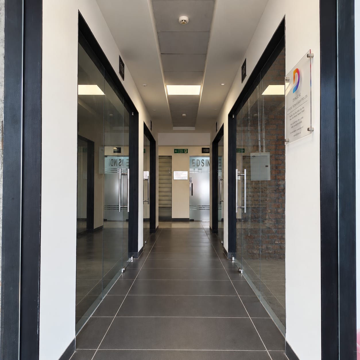 The corridor outside the Dynoz office, glass doors either side and the plaque by the entrance.